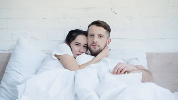 Scared woman watching movie with boyfriend near popcorn on bed — Stock Photo