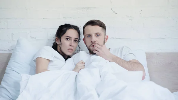 Беспокойная женщина смотрит страшный фильм с парнем возле попкорна в спальне — стоковое фото