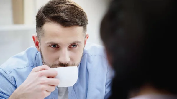 Mann trinkt Kaffee und sieht verschwommene Freundin an — Stockfoto
