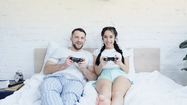 KYIV, UKRAINE - 17 JUIN 2021 : couple joyeux jouant au jeu vidéo dans la chambre à coucher — Photo de stock