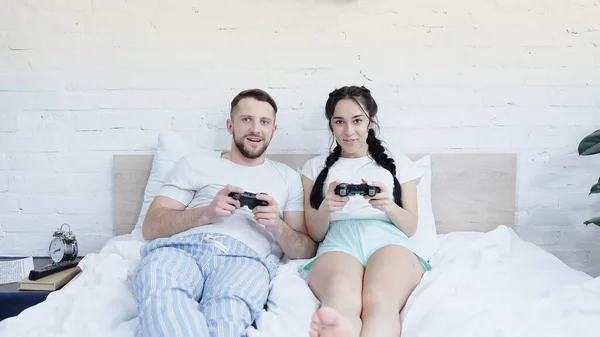 KYIV, UCRANIA - 17 de junio de 2021: pareja alegre jugando videojuegos en el dormitorio - foto de stock