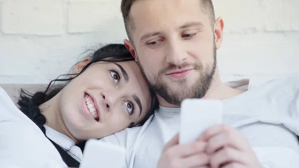 Hombre y mujer felices usando teléfonos inteligentes en casa - foto de stock