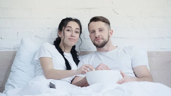 Счастливая молодая пара с попкорном смотреть кино в постели — стоковое фото