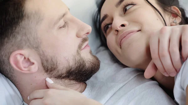 Glückliche brünette Frau schaut ihren bärtigen Freund an, während sie sich auf dem Bett ausruht — Stockfoto