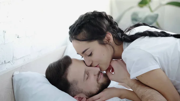 Junge brünette Frau küsst Nase ihres bärtigen Freundes im Schlafzimmer — Stockfoto