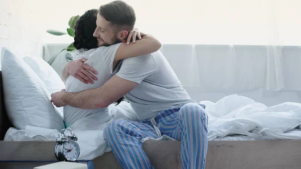 Bearded man sitting on bed and hugging girlfriend — Photo de stock