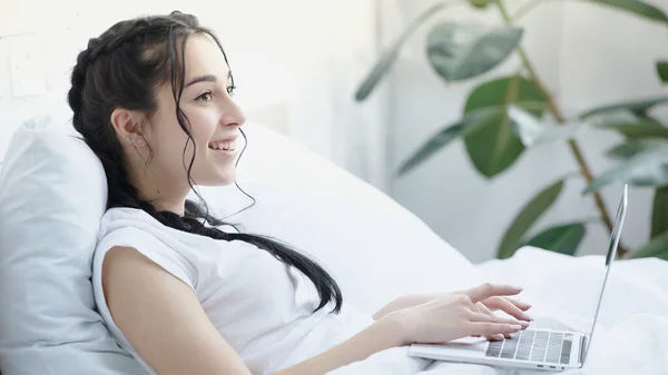 Glückliche Freiberuflerin mit Zöpfen mit Laptop im Schlafzimmer — Stockfoto