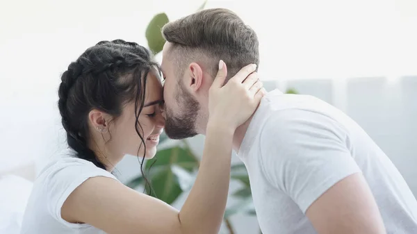 Bearded man kissing forehead of smiling girlfriend — Stock Photo