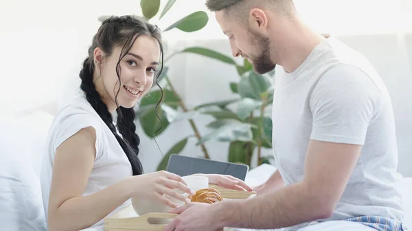 Bearded man bringing breakfast to cheerful girlfriend with braids in bed — Stock Photo