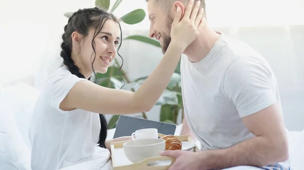 Bearded man bringing breakfast to pretty girlfriend with braids in bed — Stock Photo