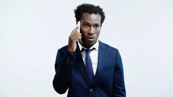 Curly african american businessman in suit talking on smartphone isolated on blue — Stock Photo