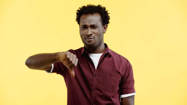 Незадоволений кучерявий афроамериканський чоловік у сорочці, показуючи великий палець вниз ізольовано на жовтому — стокове фото