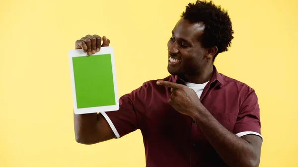 Hombre afroamericano feliz en camisa borgoña apuntando a la tableta digital con pantalla verde aislada en amarillo - foto de stock