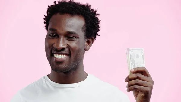 Feliz homem americano africano em branco t-shirt segurando dólares isolados em rosa — Fotografia de Stock