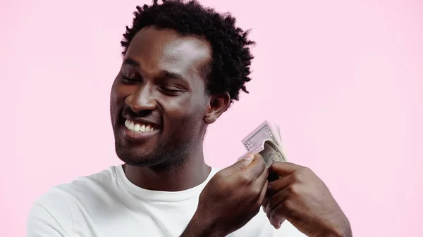 Sorridente homem americano africano em branco t-shirt segurando dólares isolados em rosa — Fotografia de Stock
