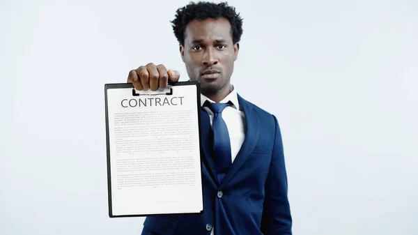 Serious african american businessman holding clipboard with contract isolated on blue — Stock Photo