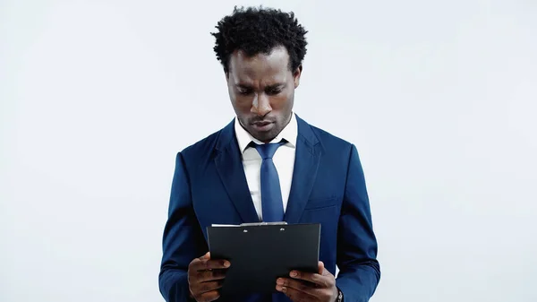 Hombre de negocios afroamericano serio mirando portapapeles aislado en azul - foto de stock
