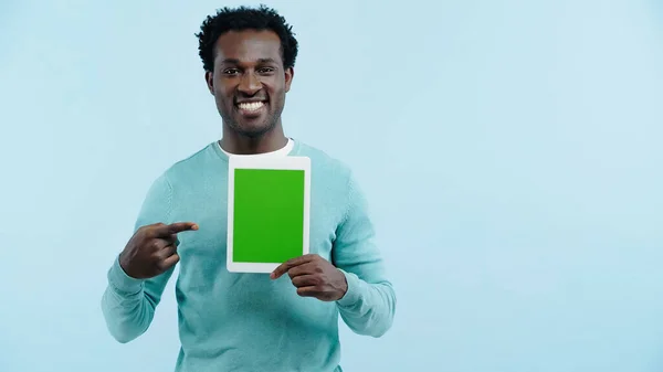 Felice uomo africano americano che punta con il dito al tablet digitale con schermo verde isolato su blu — Foto stock