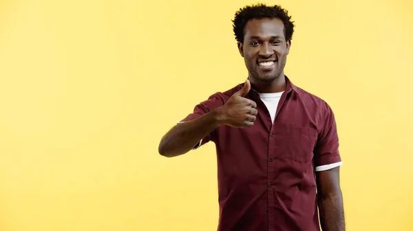 Positive young african american man in red shirt showing thumb up isolated on yellow — Stock Photo