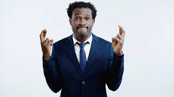 African american businessman in suit with crossed fingers isolated on blue — Stock Photo