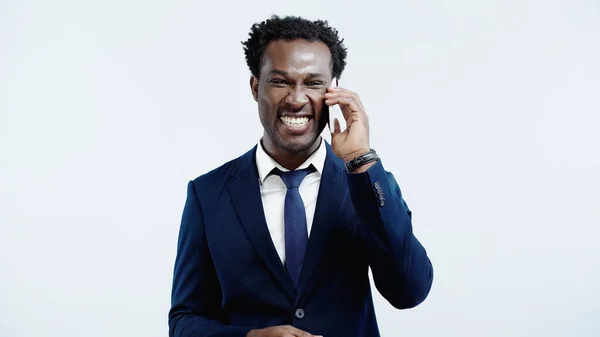 Cheerful african american businessman in suit talking on cellphone isolated on blue — Stock Photo