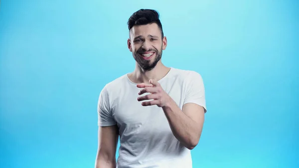 Cheerful man laughing while pointing at camera isolated on blue — Stock Photo