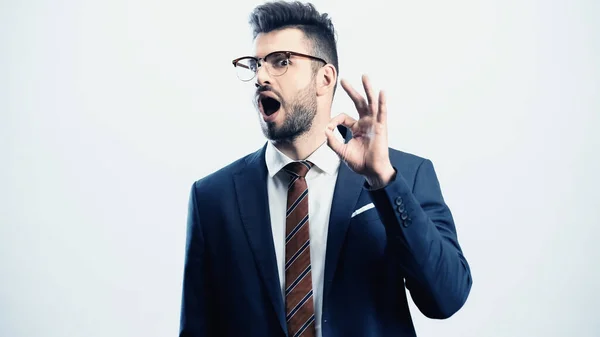 Empresário animado com a boca aberta mostrando gesto ok isolado no branco — Fotografia de Stock