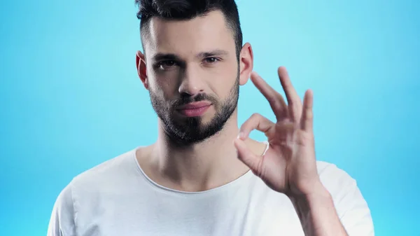 Positive young man showing okay while looking at camera isolated on blue — Stock Photo