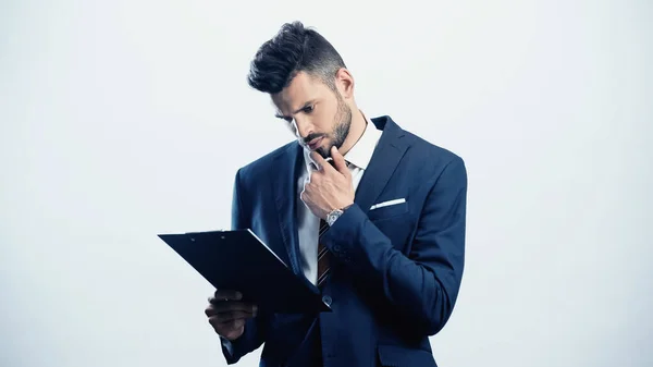 Thoughtful businessman holding hand near face while looking at clipboard isolated on white — Stock Photo