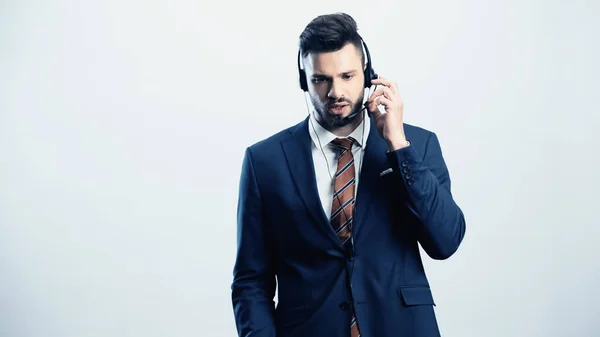 Serious call center operator in suit adjusting headset isolated on white — Stock Photo