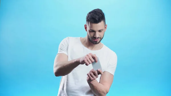 Jeune homme jeu sur téléphone mobile isolé sur bleu — Photo de stock