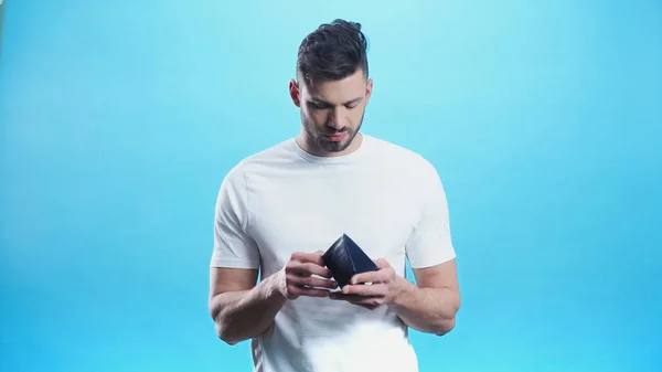 Hombre joven en camiseta blanca mirando en la cartera aislado en azul - foto de stock