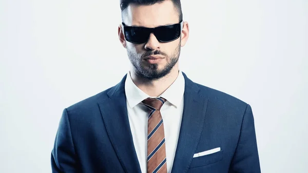 Joven hombre de negocios en traje y gafas de sol oscuras mirando a la cámara aislada en blanco - foto de stock