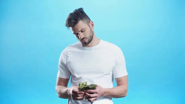 Junger Mann in weißem T-Shirt, der Dollars auf blauem Grund zählt — Stockfoto