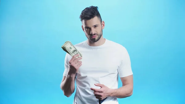 Joven mirando a la cámara mientras muestra el dinero aislado en azul - foto de stock