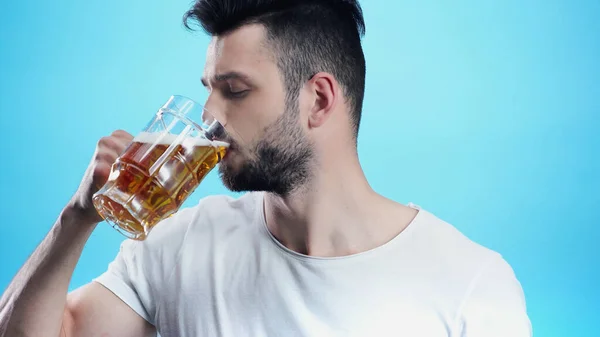 Молодий чоловік п'є холодне пиво ізольовано на синьому — Stock Photo