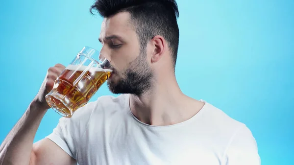 Jovem bebendo cerveja fria isolada no azul — Fotografia de Stock