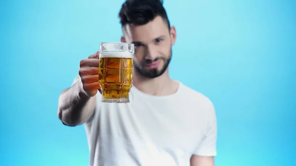 Hombre borroso con taza de cerveza fría mirando a la cámara aislada en azul - foto de stock