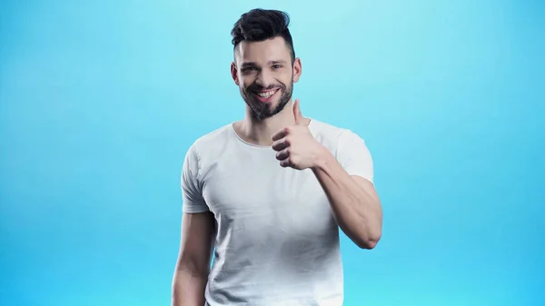 Sorrindo homem olhando para a câmera e mostrando polegar para cima isolado em azul — Fotografia de Stock