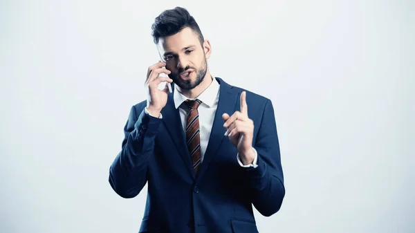 Serious businessman pointing up with finger while calling on smartphone isolated on white — Stock Photo