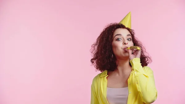 Bouclé jeune femme soufflant partie corne isolé sur rose — Photo de stock