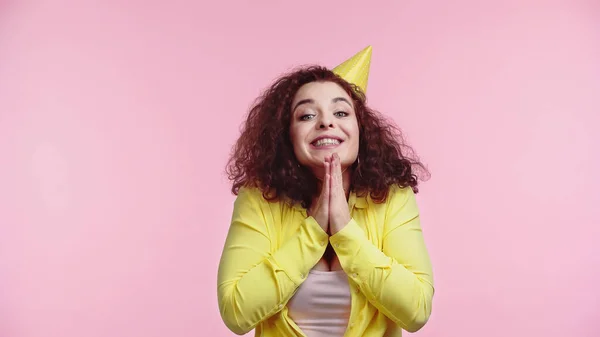 Excited young woman in party cap with praying hands isolated on pink — Stock Photo