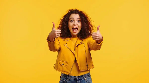 Здивована молода жінка, показуючи великі пальці вгору ізольовано на жовтому — стокове фото