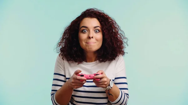 KYIV, UKRAINE - JUNE 30, 2021: young tensed woman holding pink joystick and biting lips while playing video game isolated on blue — Stock Photo