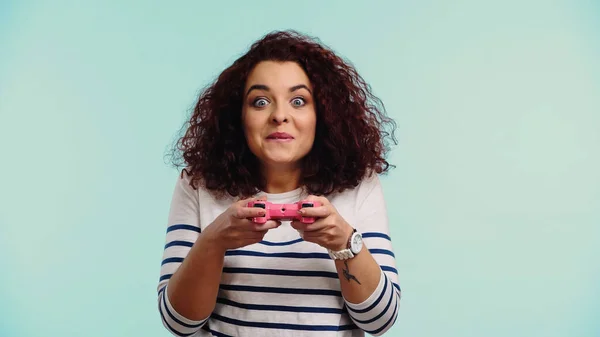 KYIV, UCRANIA - 30 de junio de 2021: mujer excitada sosteniendo un joystick rosa y jugando a un videojuego aislado en azul — Stock Photo