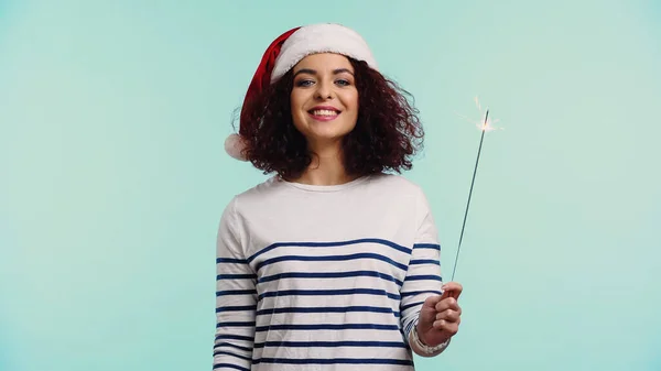 Felice giovane donna in cappello di Babbo Natale tenendo sparkler isolato su blu — Foto stock