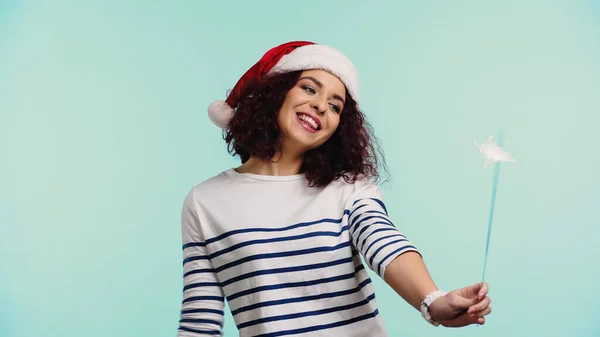 Радісна молода жінка в капелюсі Санта тримає іскриста ізольована на синьому — стокове фото