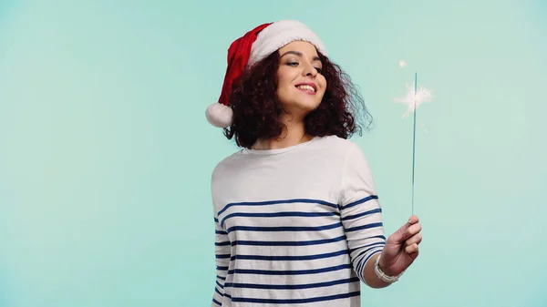 Sorrindo jovem mulher em santa chapéu segurando sparkler isolado em azul — Fotografia de Stock