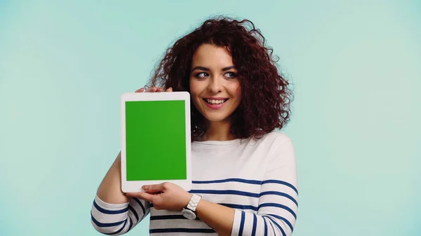 Fröhliche junge Frau hält digitales Tablet mit grünem Bildschirm isoliert auf blauem Hintergrund — Stockfoto