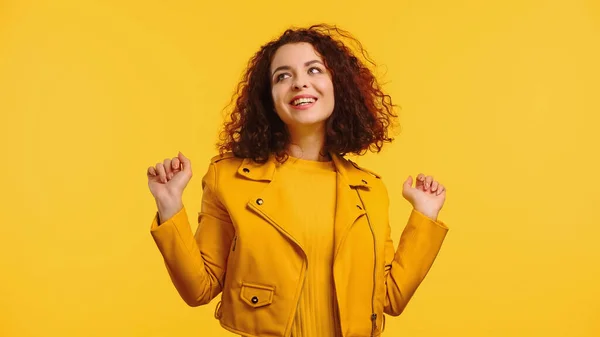 Pleased curly and young woman in leather jacket isolated on yellow — Stock Photo